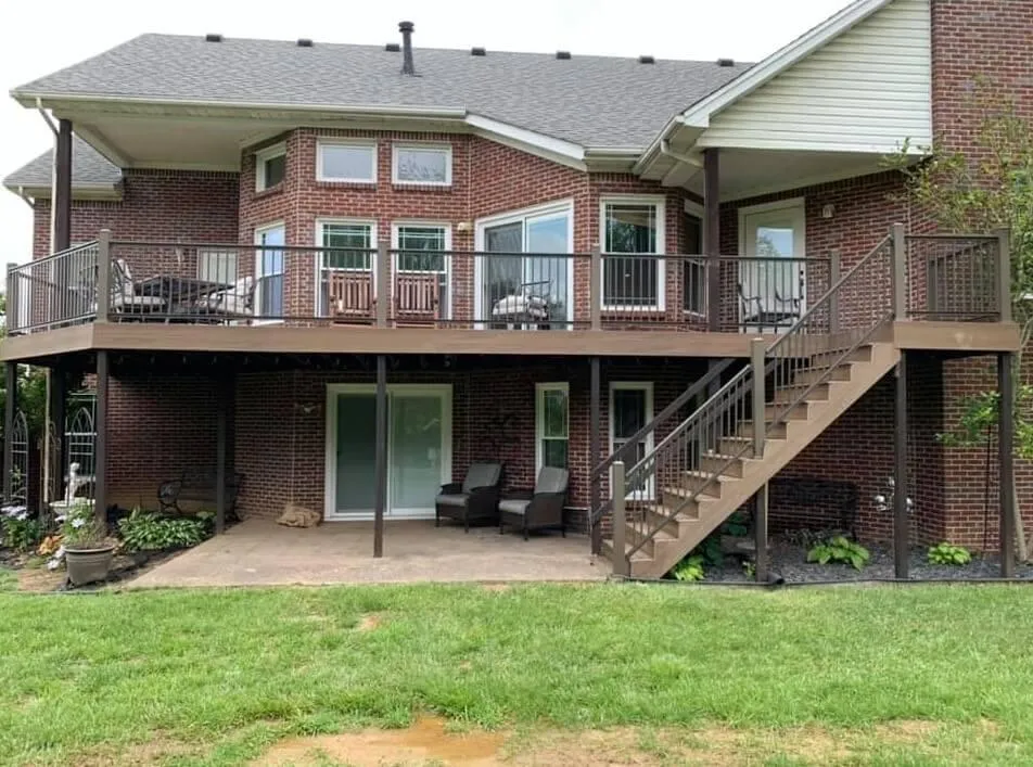 Two-story brick house with a large elevated wooden deck featuring railings, stairs, and a covered patio space below.