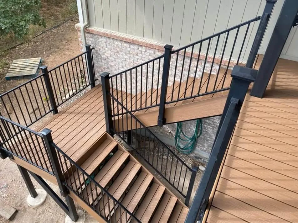 Wooden deck staircase with black metal railings, featuring multiple landings and leading down the side of a house.