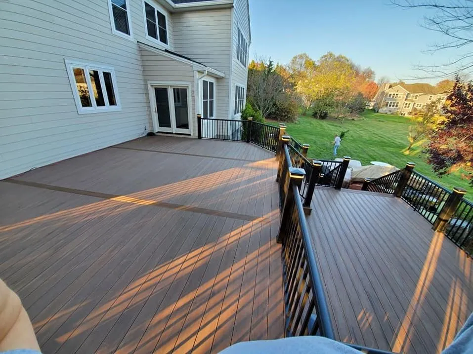 Spacious finished backyard deck attached to a house, with brown flooring and black railings overlooking a grassy yard.