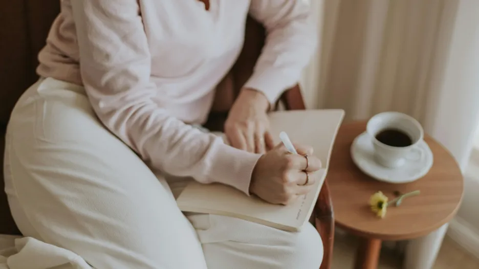 Woman journaling with coffee as part of a daily routine for building confidence