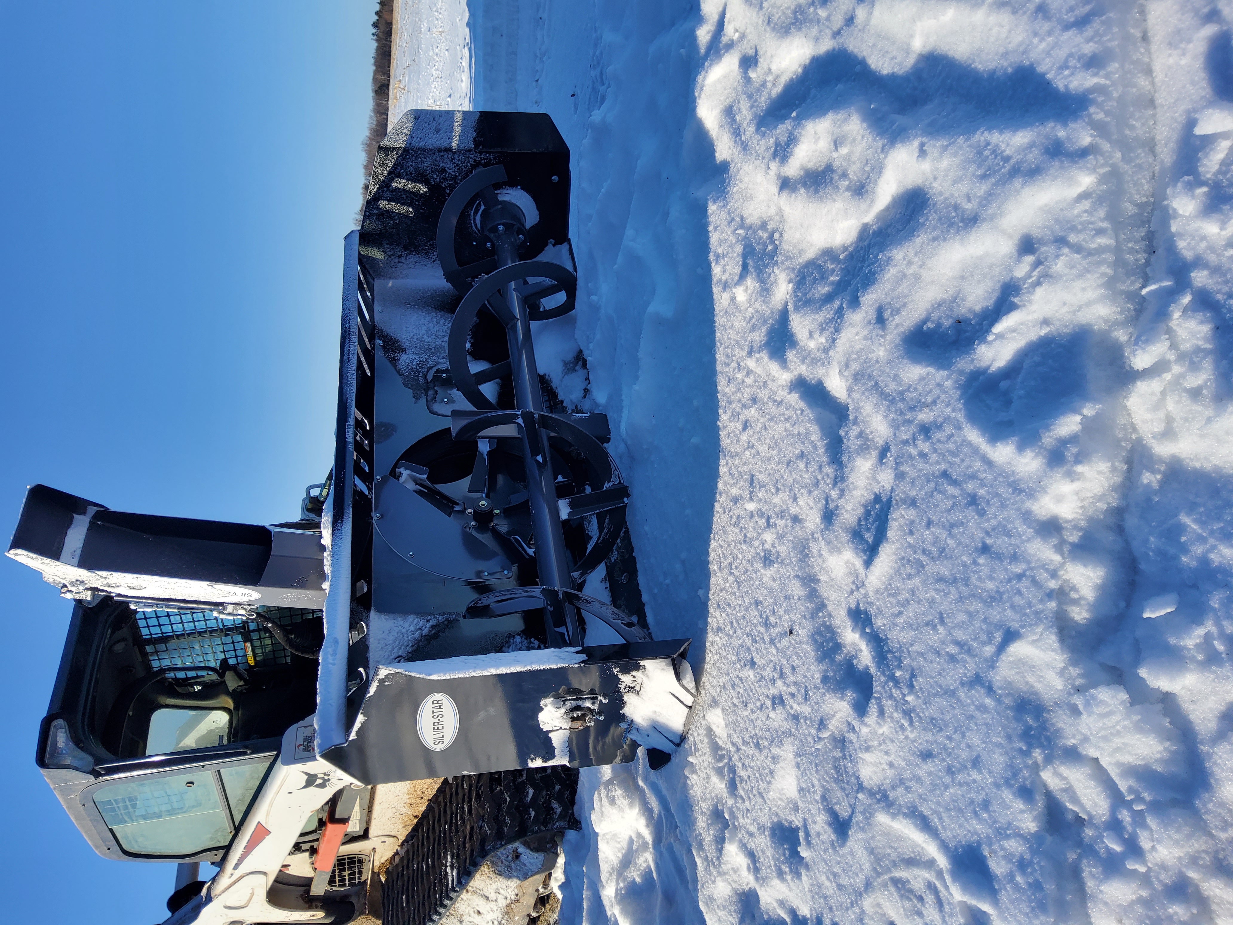 Skid steer loaders with various attachments on a gravel lot