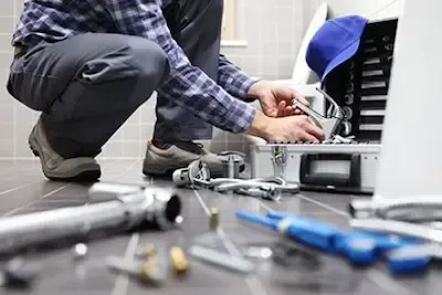 Plumber crouched on tile floor servicing appliance connections with tools spread nearby