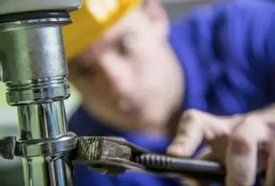 Yellow hard hat plumber focused on tightening pipe fitting during plumbing repair in Pickerington