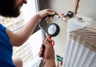 Plumber using pressure gauge to test radiator valve connection during leak detection in Pickerington