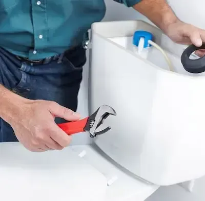 Plumber adjusting toilet tank supply line with adjustable wrench during toilet repair in Pickerington