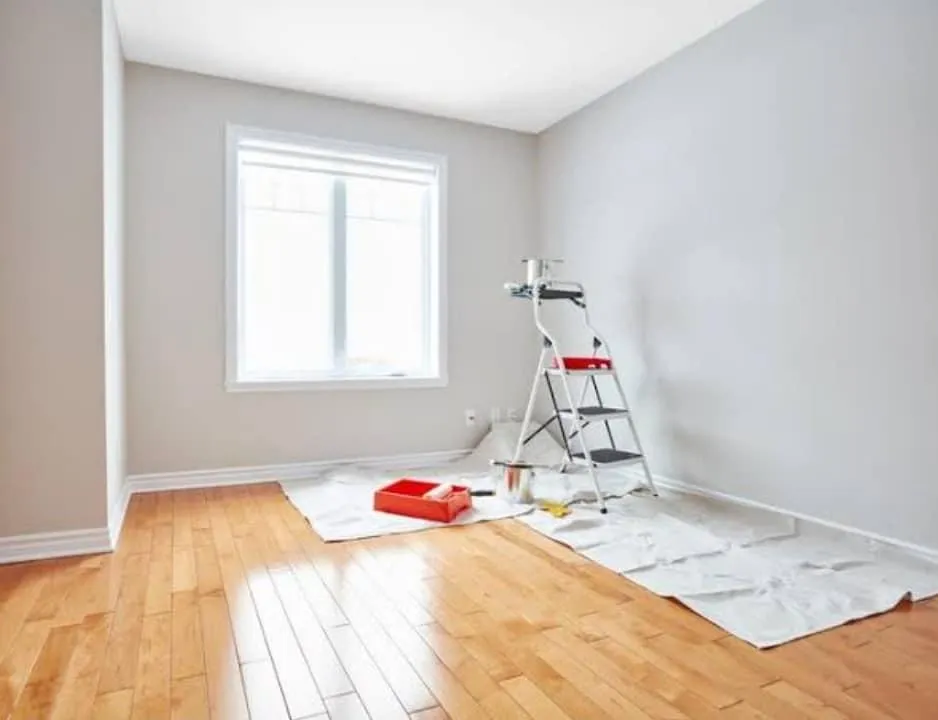 Clean interior room setup for painting with drop cloth, ladder, and roller trays on timber floor