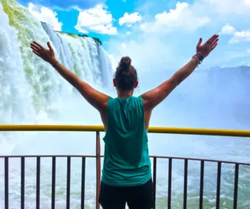 Woman with arms raised in awe facing Iguazu Falls on the Argentina-Brazil border, surrounded by mist and powerful cascading waterfalls