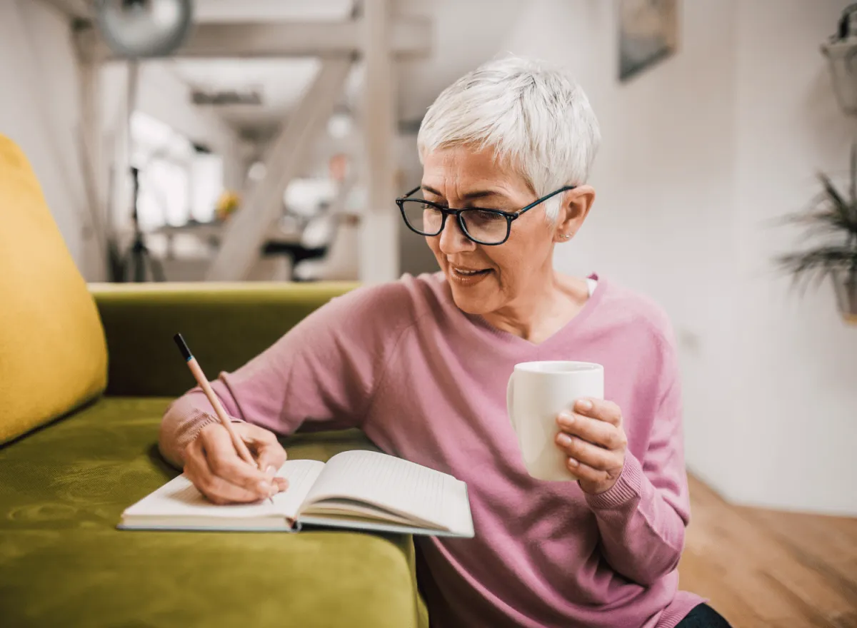 Mature woman writing book and holding cup of coffee