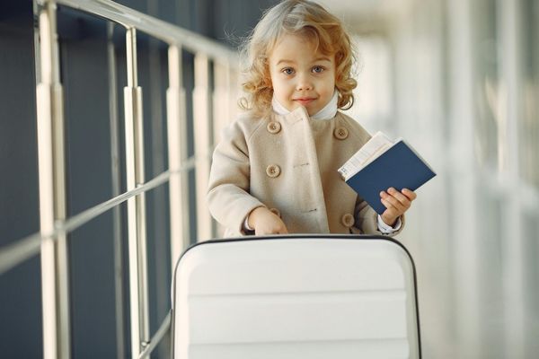 Young child holding passport and suitcase for spring break travel with notarized minor travel consent documents