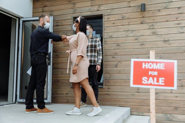 Home buyers meeting with a real estate professional outside a house during closing, highlighting document signing and notary services during peak buying season.