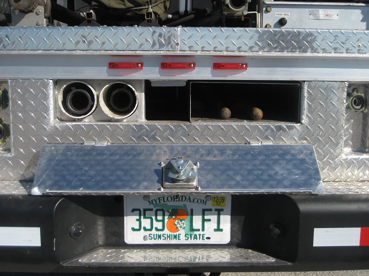 Southern Rough wildland fire truck rear showing custom between-frame-rail storage with dual suction hose tubes and underbody compartment on diamond plate bed