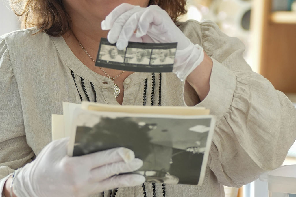 Magic Lantern Memories specialist carefully handling printed photographs and film negatives while organizing and preserving family memories.