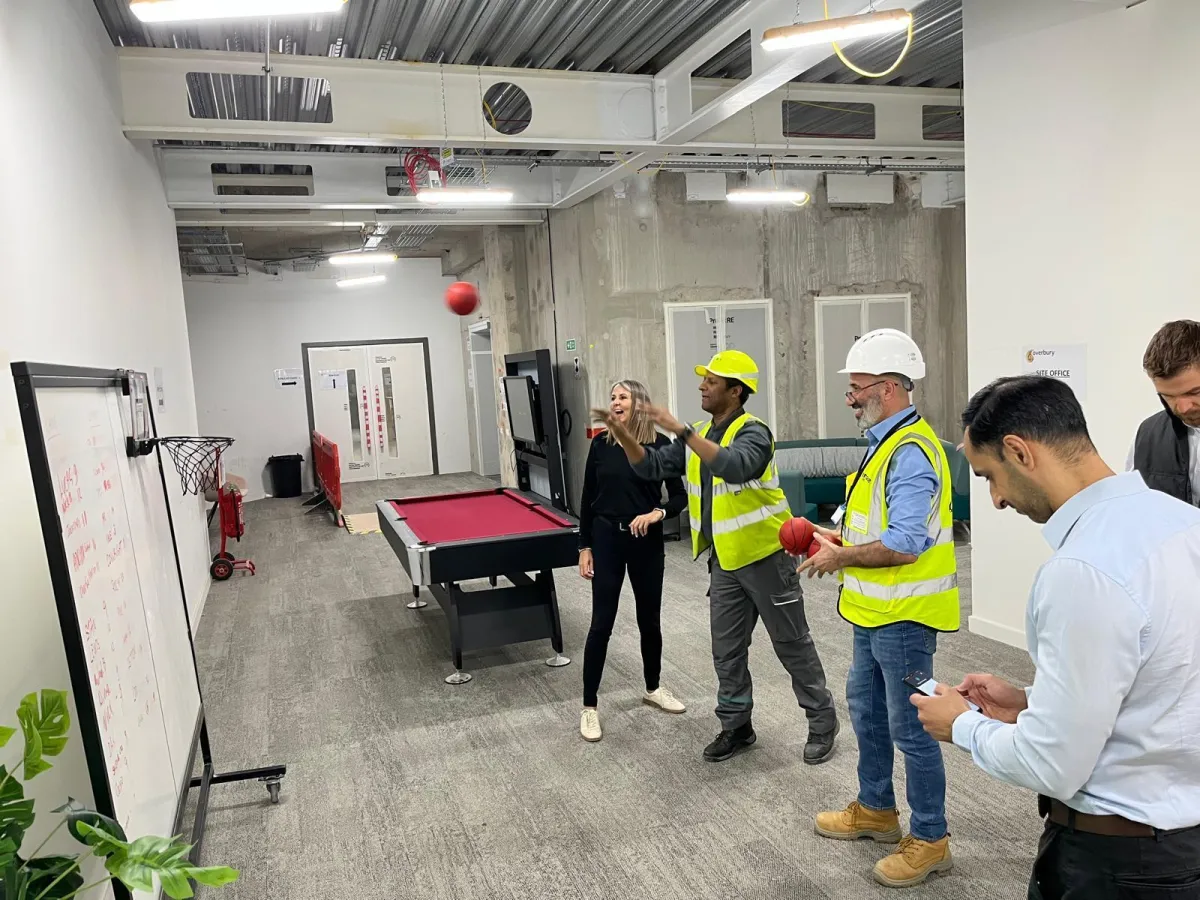 Construction workers standing by an on-site Wellbeing Cabin, engaging in conversation while wearing safety PPE.