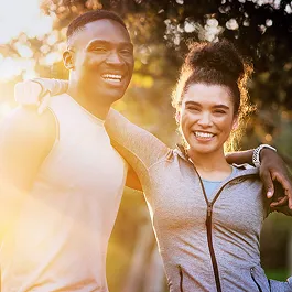 Happy couple dressed in fitness gear with arms around each other, enjoying time outdoors, representing wellness, connection, and support.