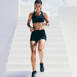 Athletic woman in black workout clothes running up bright white stairs, representing energy, progress, and physical momentum.