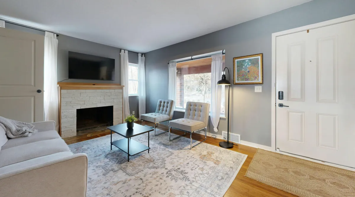 Modern living room remodel featuring stone fireplace, neutral sectional sofa, accent chairs, and large sliding glass doors leading to a landscaped backyard