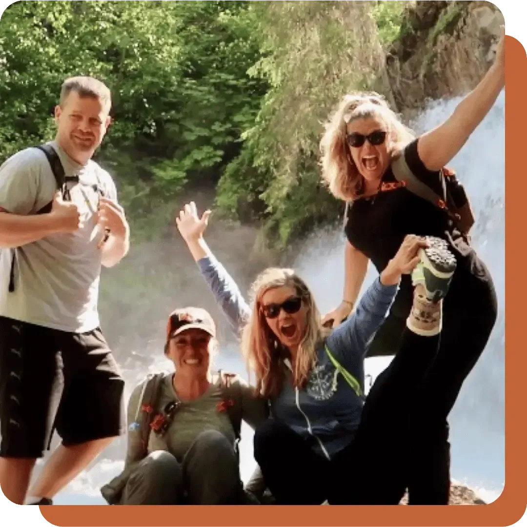 Group of four joyful hikers posing with enthusiasm in front of a waterfall, showcasing a sense of adventure and camaraderie, reflecting the spirit of personal growth and resilience emphasized in Dr. Barbara Eaton's coaching philosophy.