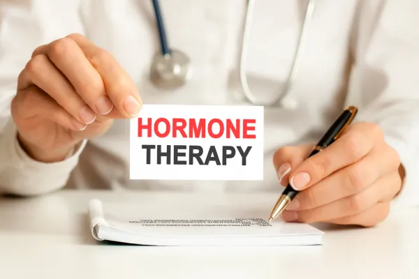 Doctor in white coat and blue gloves holding cards with the words "HORMONE" and "BALANCE," emphasizing personalized hormone replacement therapy for health optimization at Zel Vitality.
