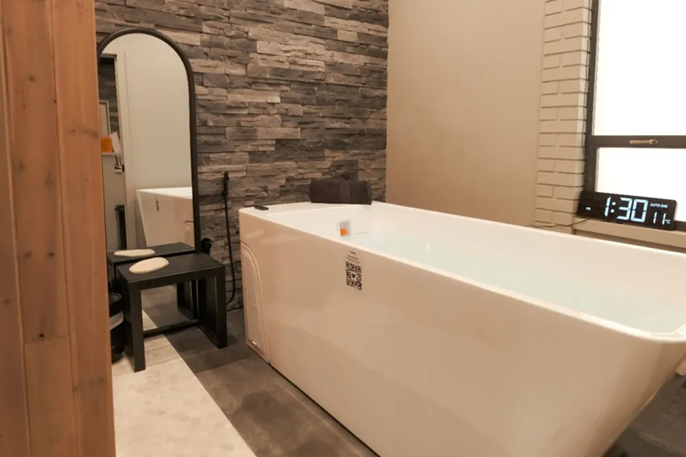 Wooden cold plunge tub surrounded by natural rocks and greenery, featuring a wooden bench for relaxation, emphasizing holistic wellness and recovery therapies.