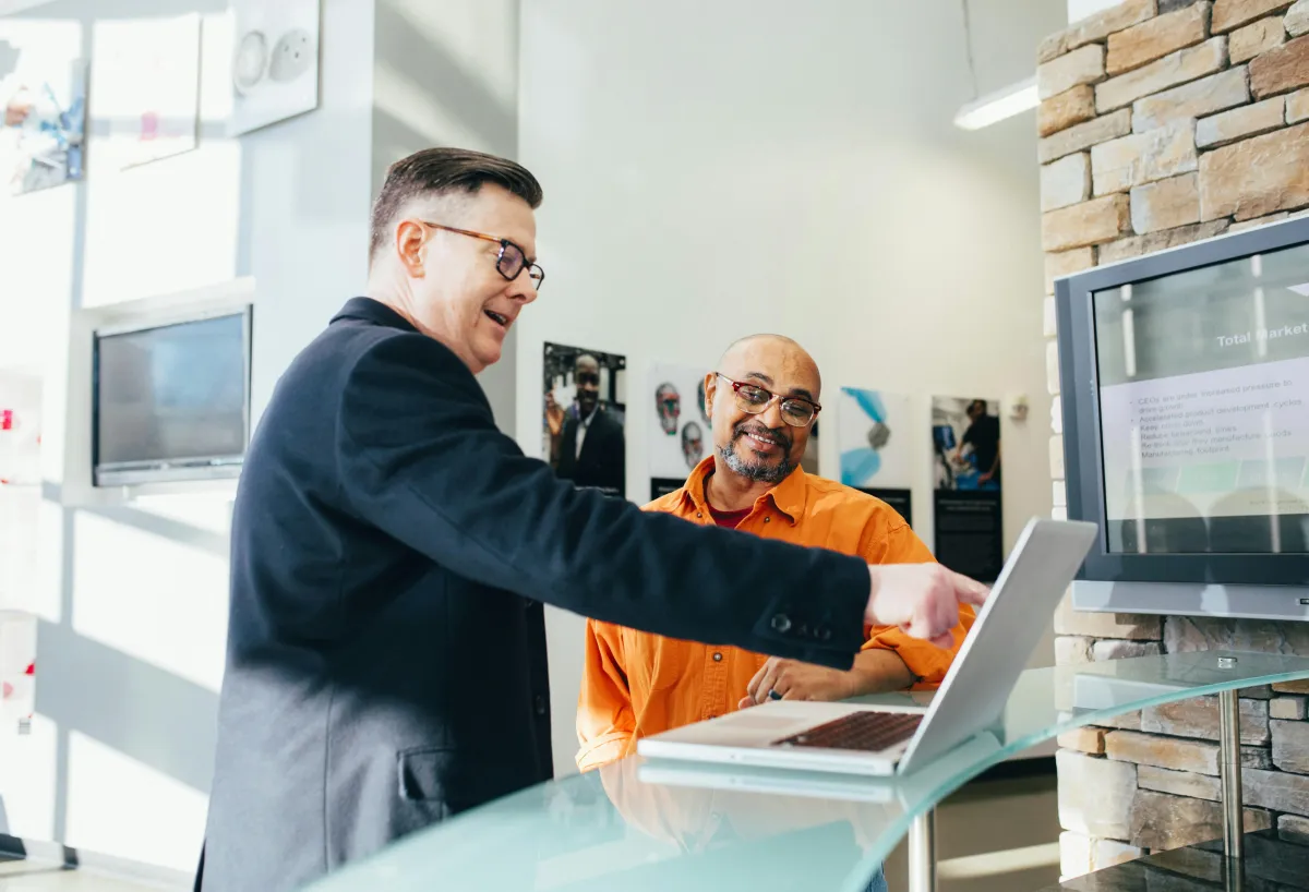 Two people in a modern office space hovering over a laptop