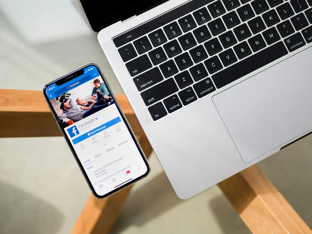 Facebook open on a cell phone next to an open laptop.