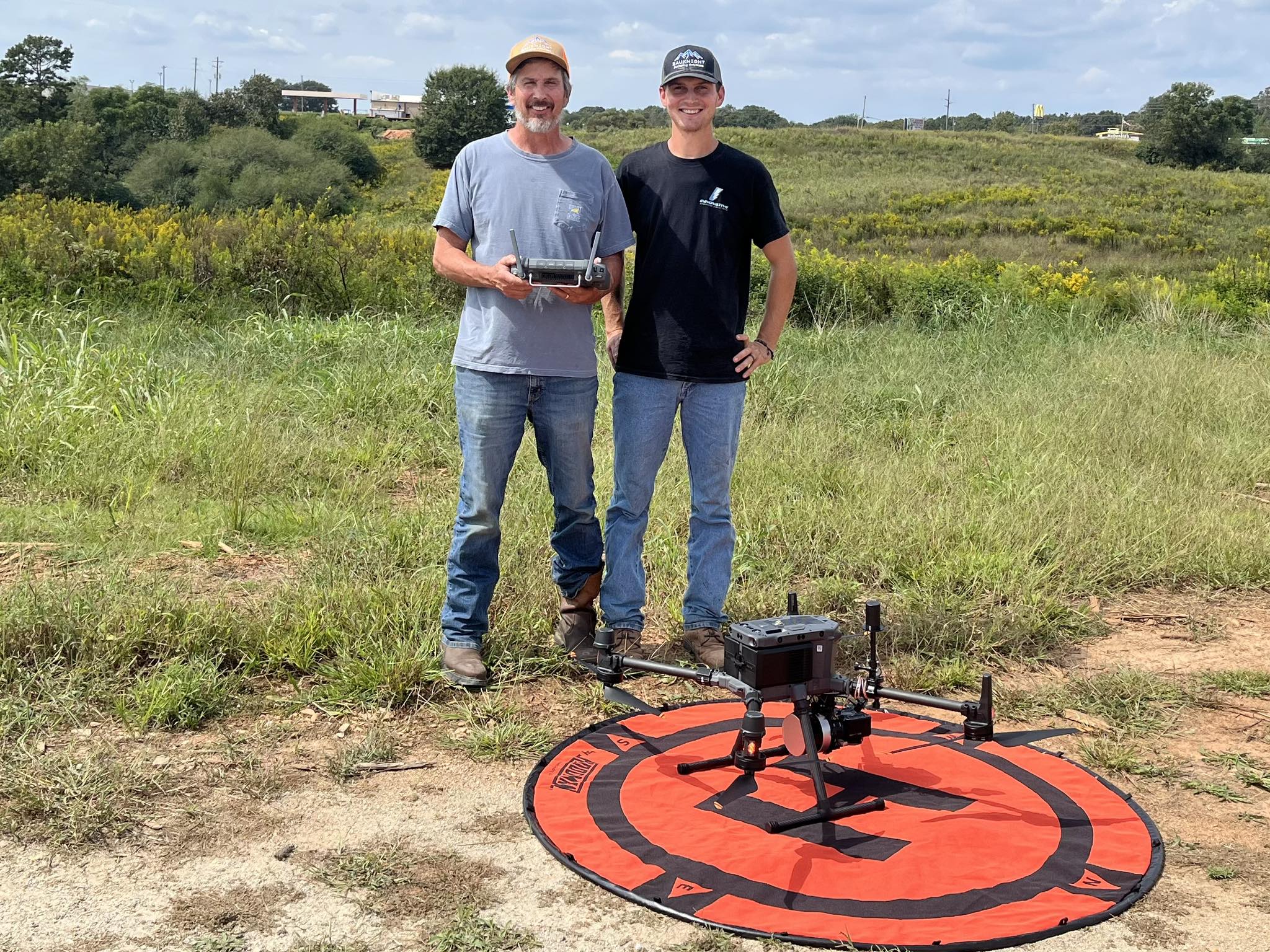 Two generations of surveyors standing side-by-side with surveying instruments.