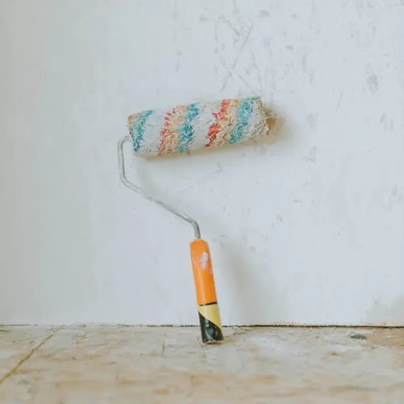 A handymans paint roller covered in paint leaning against an interior wall