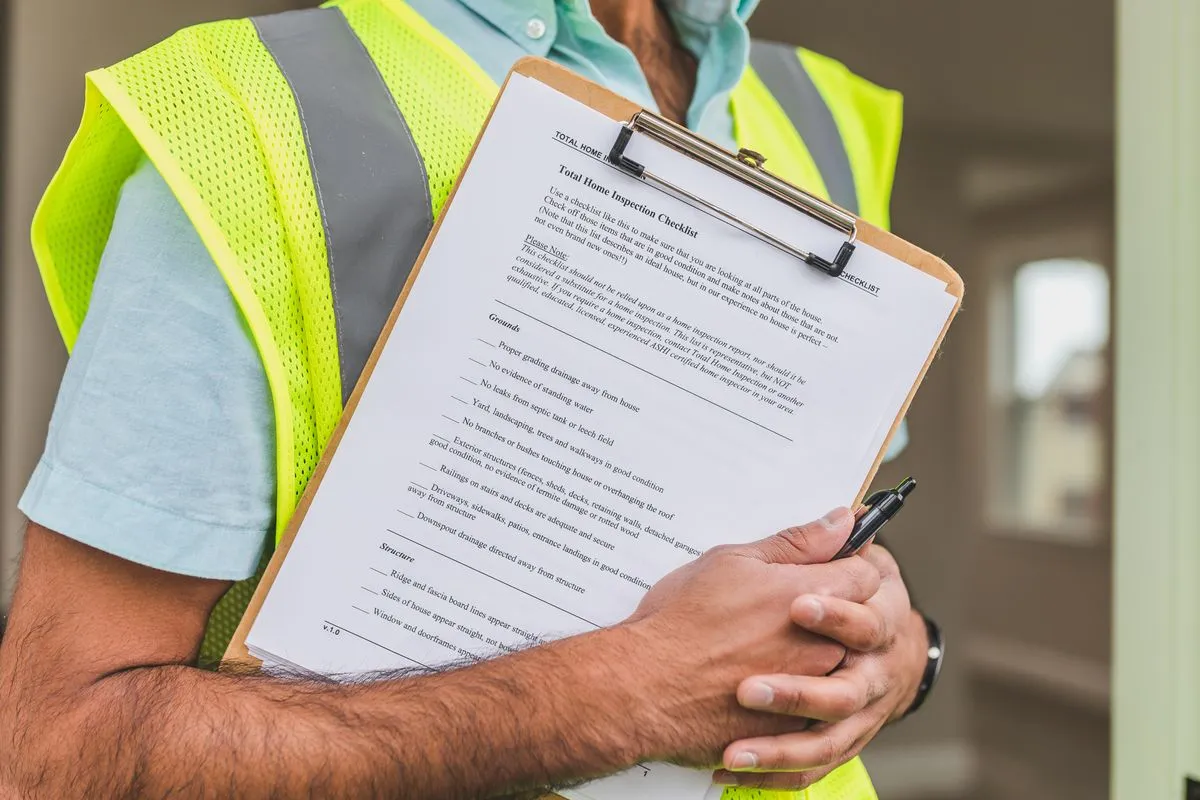 Home inspector in a safety vest holding a clipboard with a total home inspection checklist