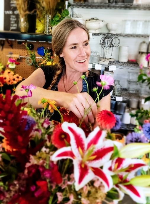 A picture of Paula Rice smiling in her studio on BeeHaven Flower Farm arranging lilies and other flowers as a cut flower expert and flower farming specialist.