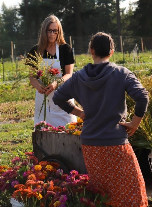 Paula Rice in the cut flower garden holding flowers and coaching and training an employee on harvesting cut flowers.