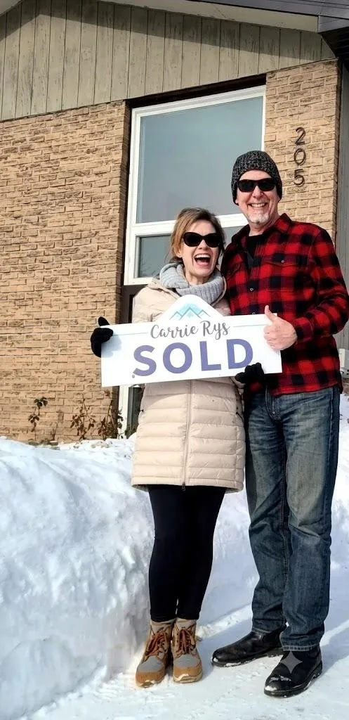 Colin Ballantyne and his wife holding a sold sign in front of an investment property purchased in winter