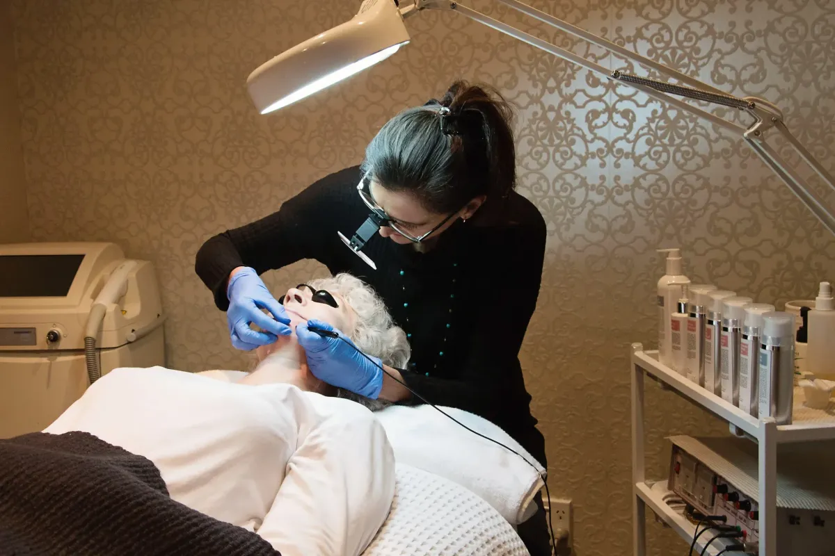 Electrolysis service image: close-up of professional performing hair removal, hands and device in frame, clinical clean styling.
