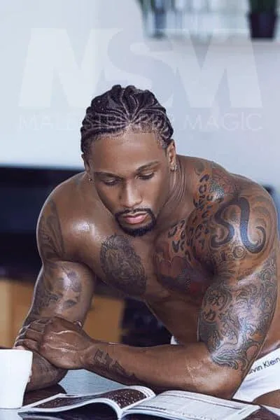 Black male stripper Pleasure engrossed in a book, showcasing cornrows and tattoos