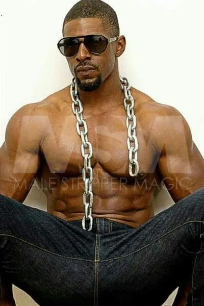 Black male stripper Dream leaning against a wall with sunglasses