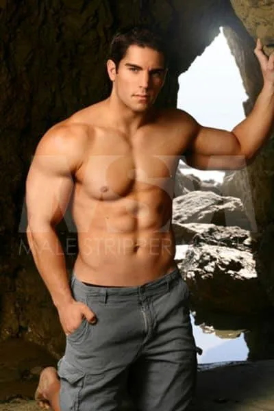 Male stripper Ethan on a beach rock formation, shirtless in cargo shorts