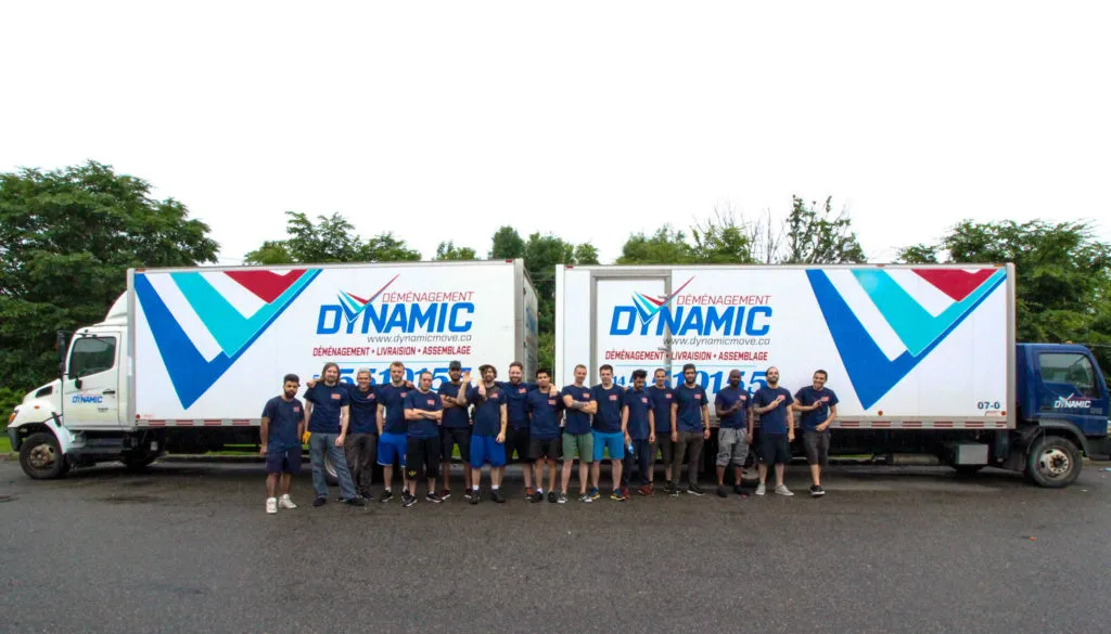 A large group photo of the Dynamic moving team wearing navy blue shirts, standing in front of two white moving trucks.