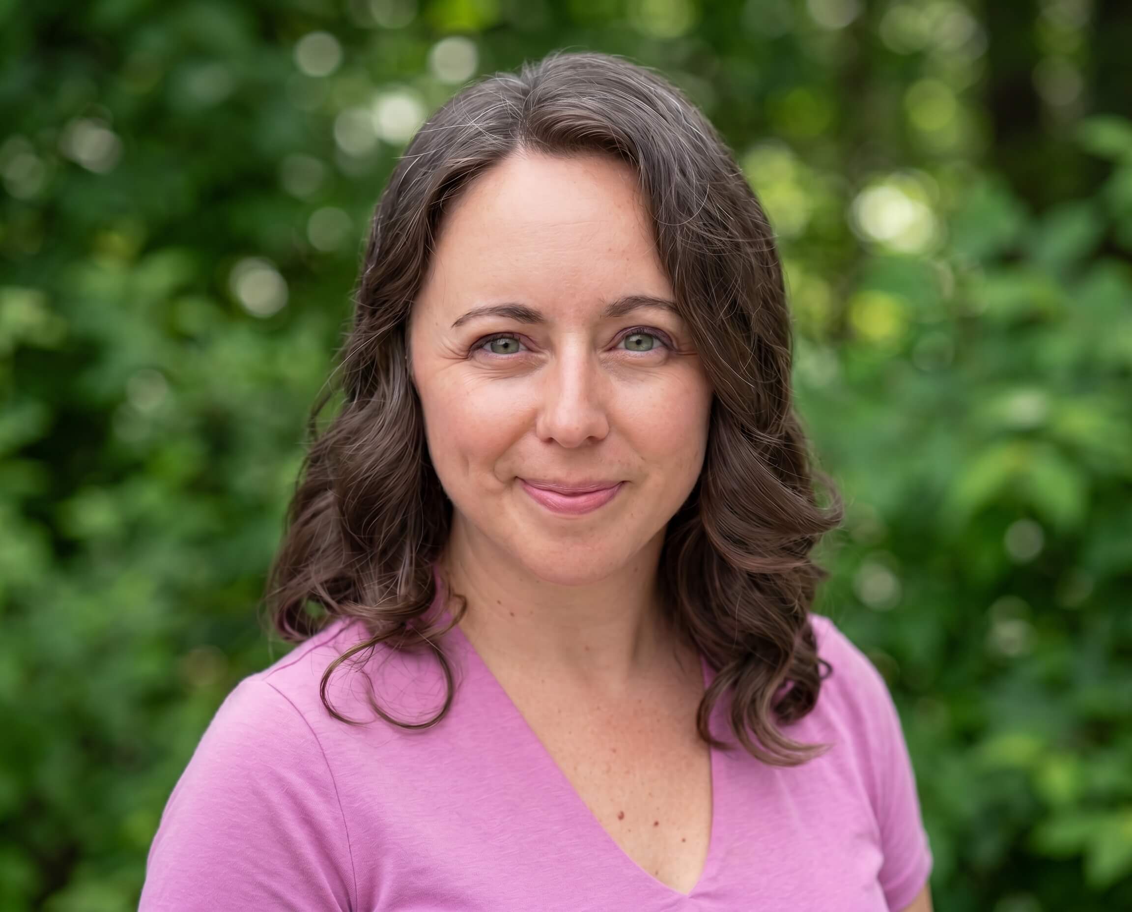 Chelsea, US trademark attorney, in a light pink shirt standing in front of vibrant green bushes— trademark protection for business owners and thought leaders