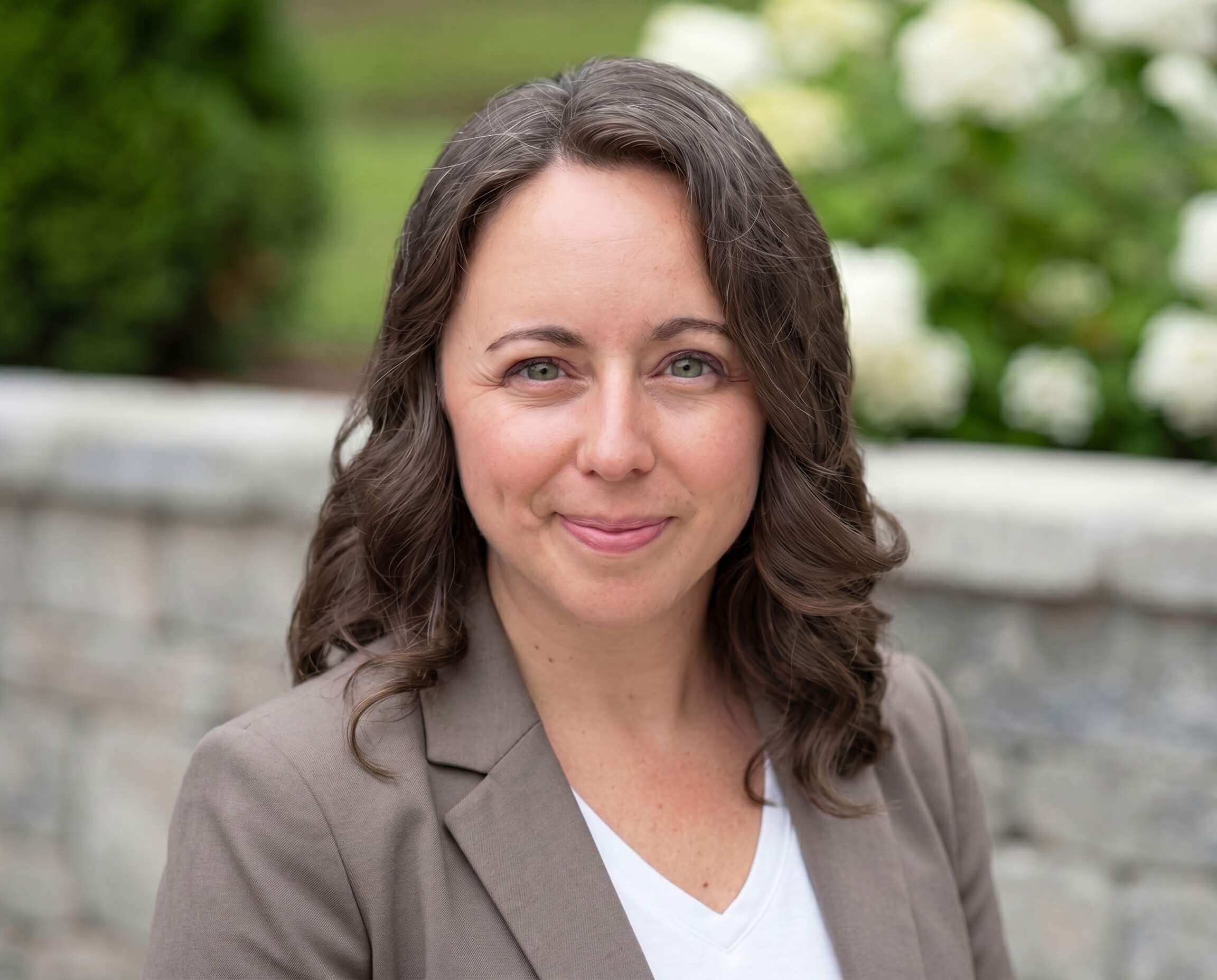 Chelsea, US trademark attorney, in a tan blazer and white blouse standing in front of a gray rockwall outside — trademark protection for business owners and thought leaders