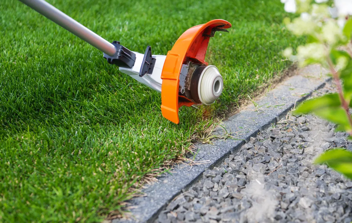 weed whacker edging grass next to concrete walkway
