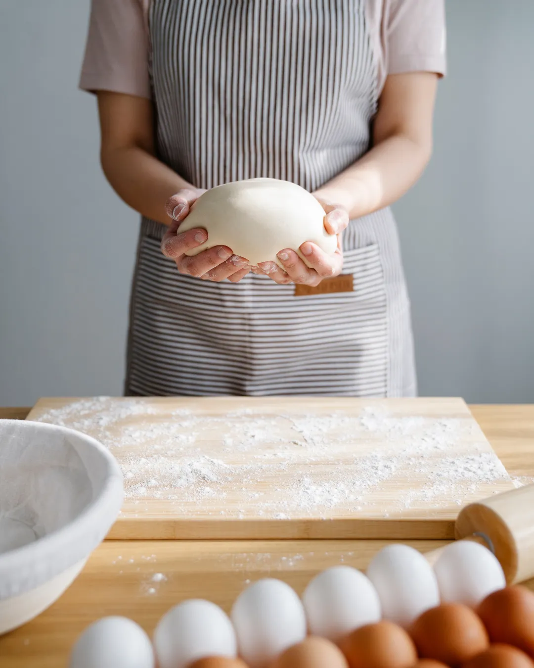baker holding a sourdough ball in her hand with a cutting bord nder and eggs