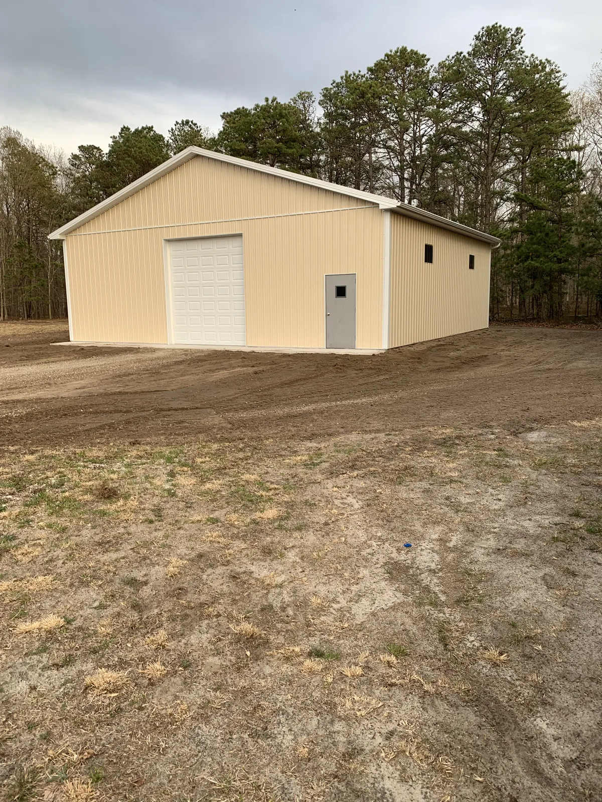 Tan post-frame building with a tall white overhead door