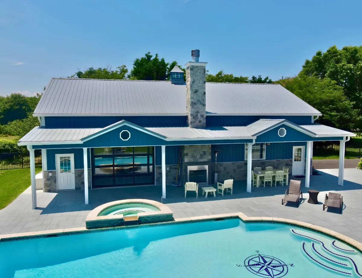 Blue pool house with stone accents and a covered patio beside a swimming pool