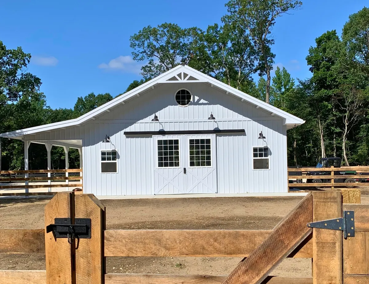 White horse barn with a metal roof and covered side area