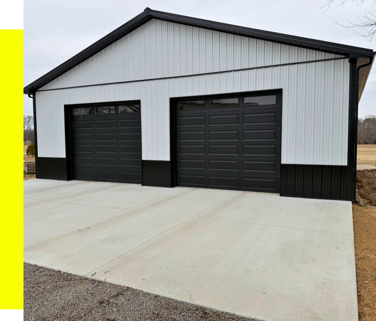 White two-bay pole garage with black doors and a concrete apron