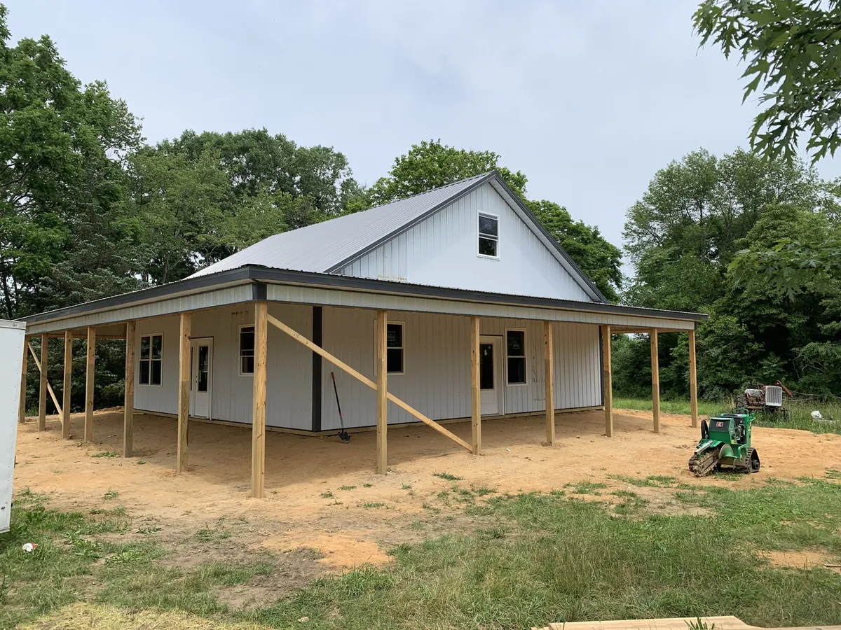 White barn-style building with residential windows and a wraparound porch under construction