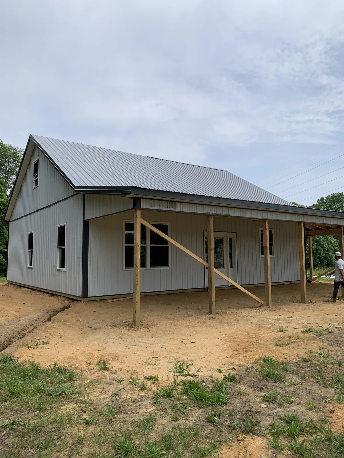 Side view of a white barn-style building with a covered porch during construction