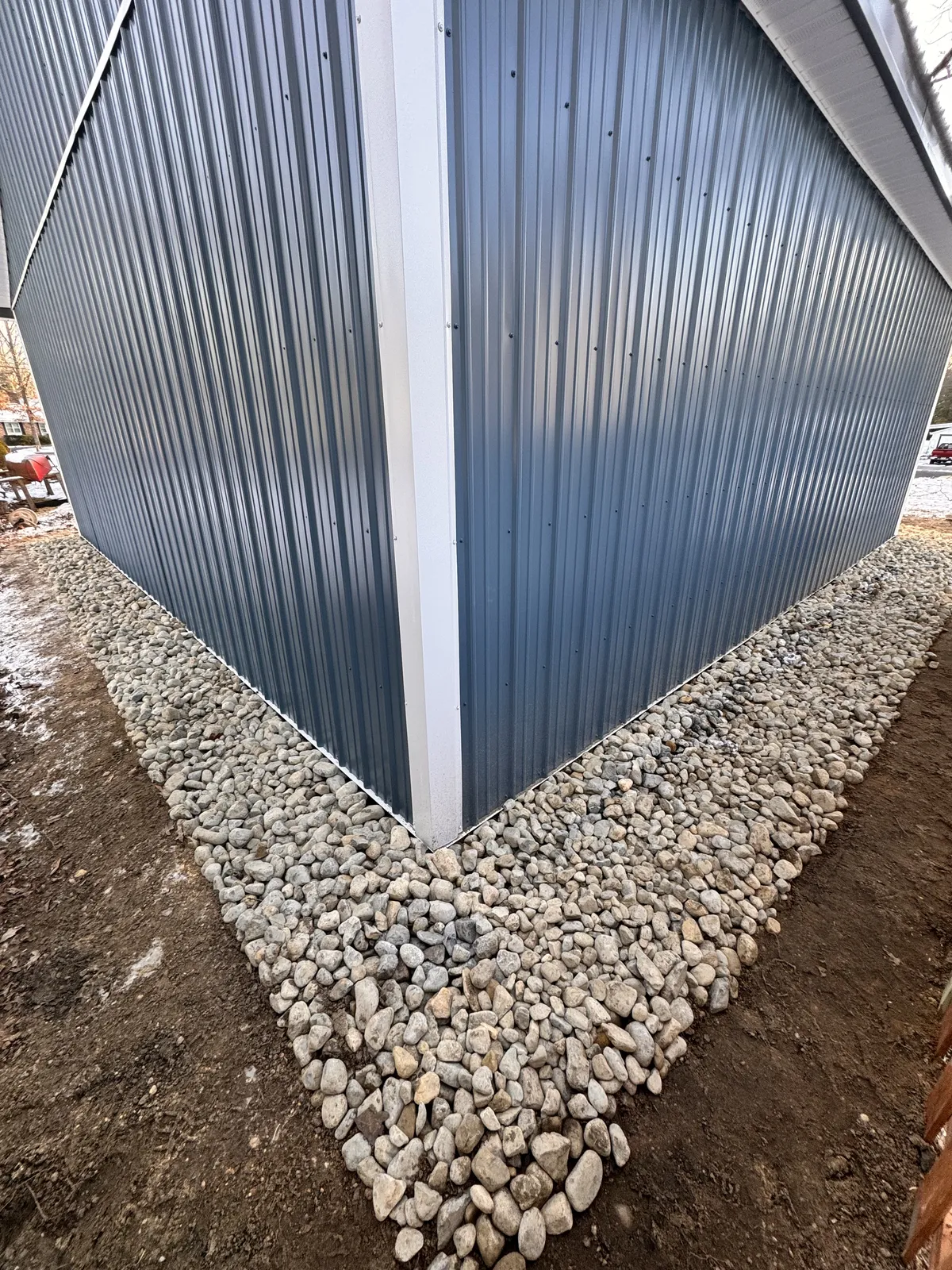 Blue metal siding with white corner trim and drainage stone at the base
