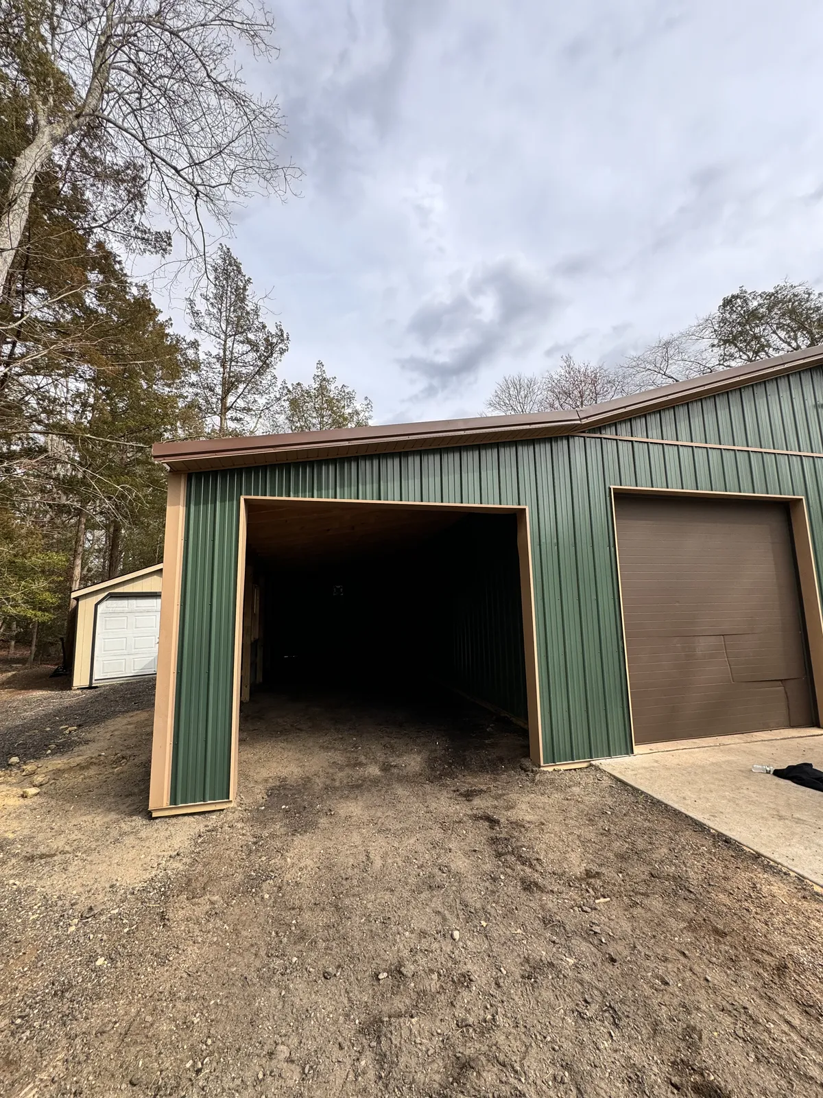 Green metal garage with tan trim and an open vehicle bay during site finishing