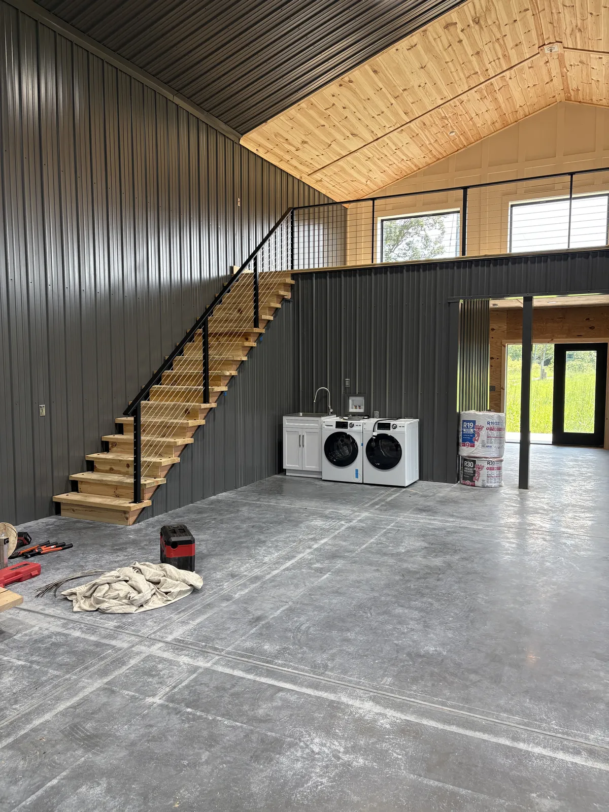 Post-frame interior with wood stairs, loft, and concrete floor during buildout