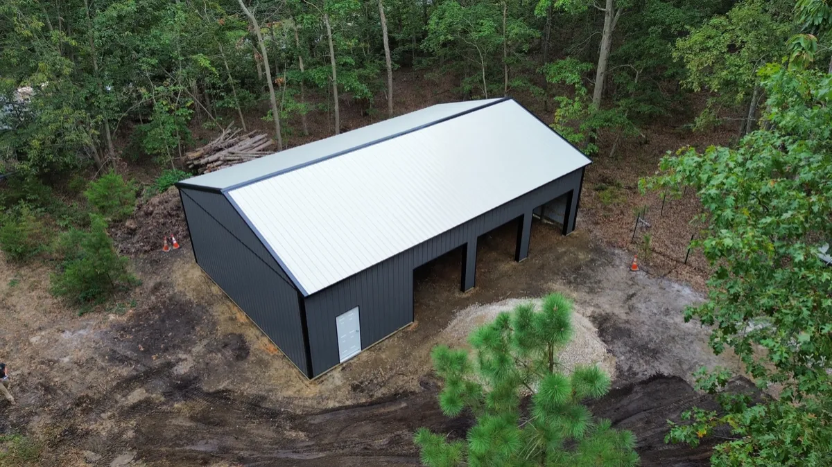 Aerial view of a charcoal three-bay pole building in a wooded setting